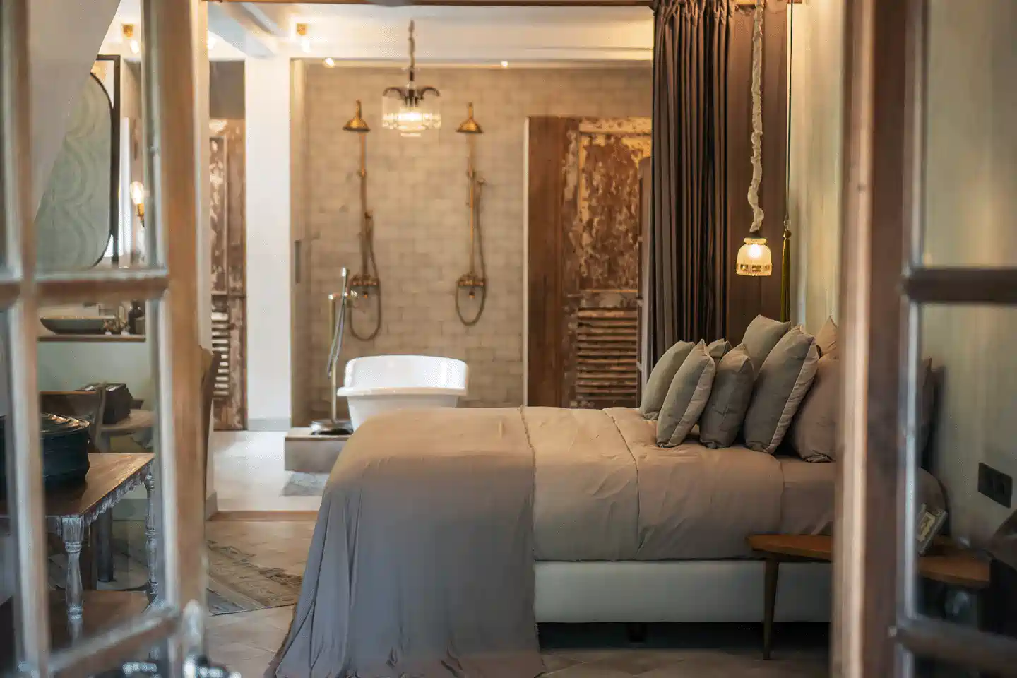 Luxurious bedroom at Balquisse Heritage Hotel, a boutique hotel in Bali, featuring a soft grey bed, freestanding bathtub, and dual rainfall showers in rustic Balinese décor.