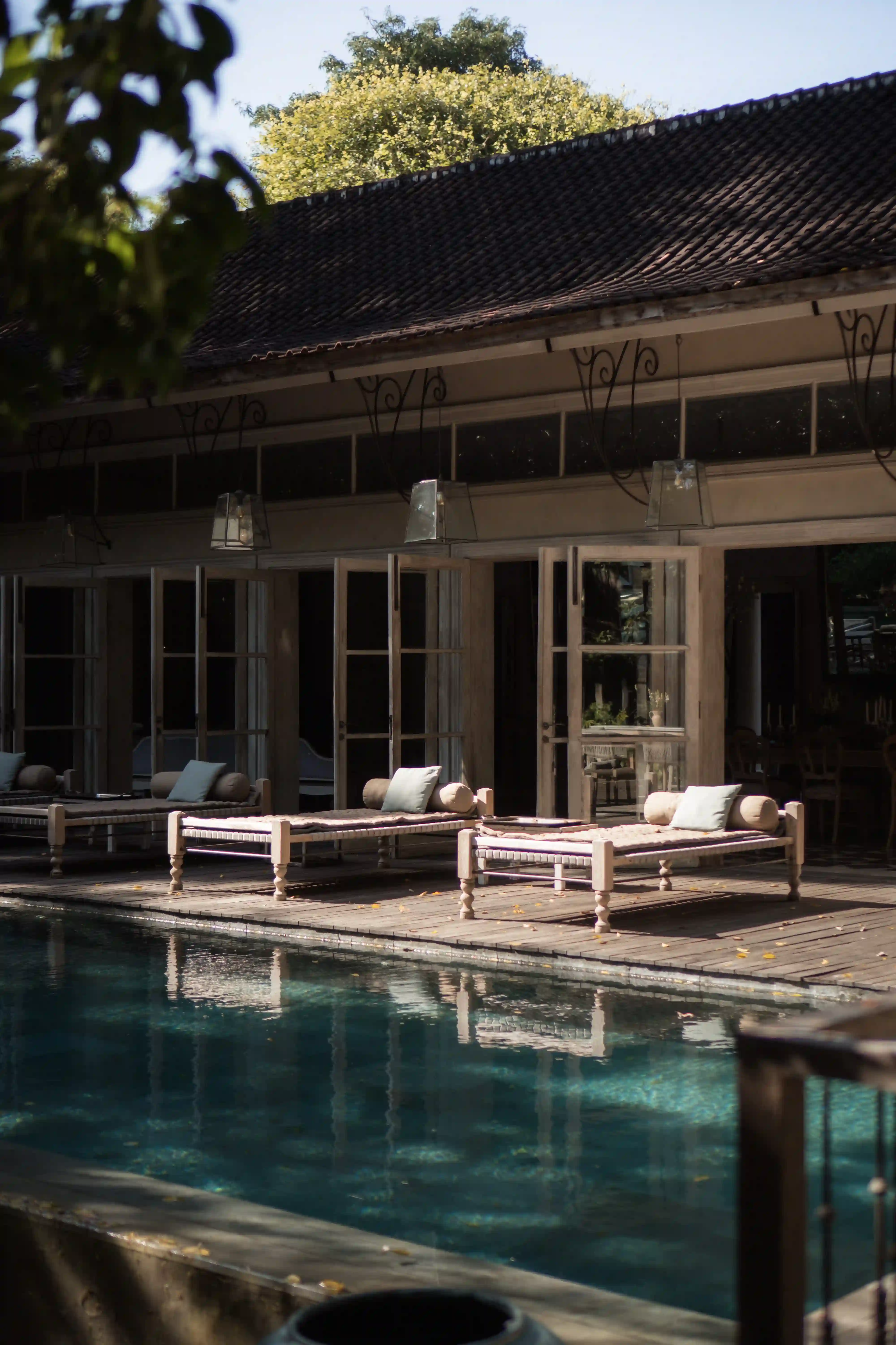 Cozy red pool beds by the private swimming pool at Balquisse Heritage Hotel Jimbaran Bali, surrounded by lush tropical garden scenery.