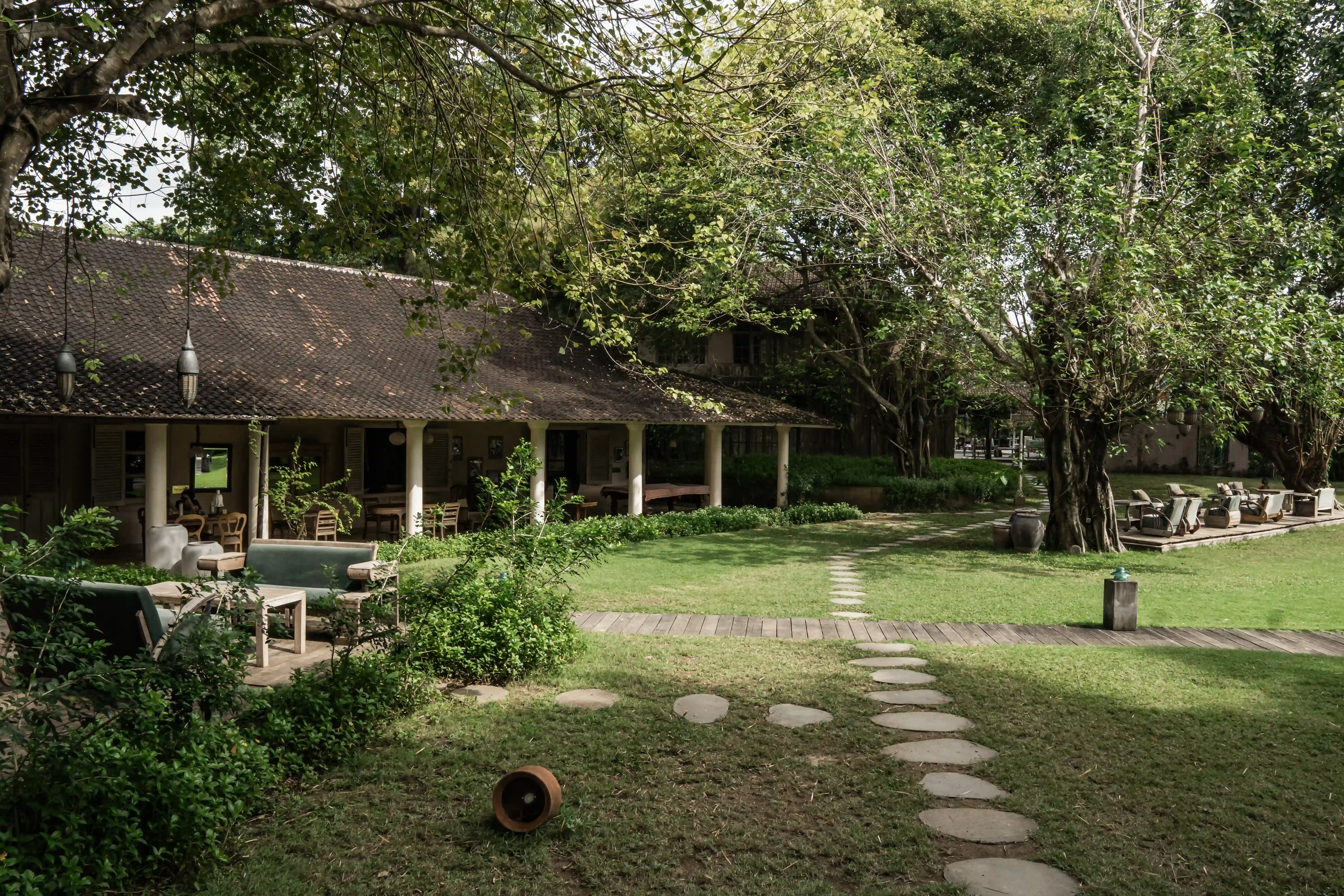 Wooden path in the lush tropical garden of Balquisse Heritage Hotel in Jimbaran, Bali.