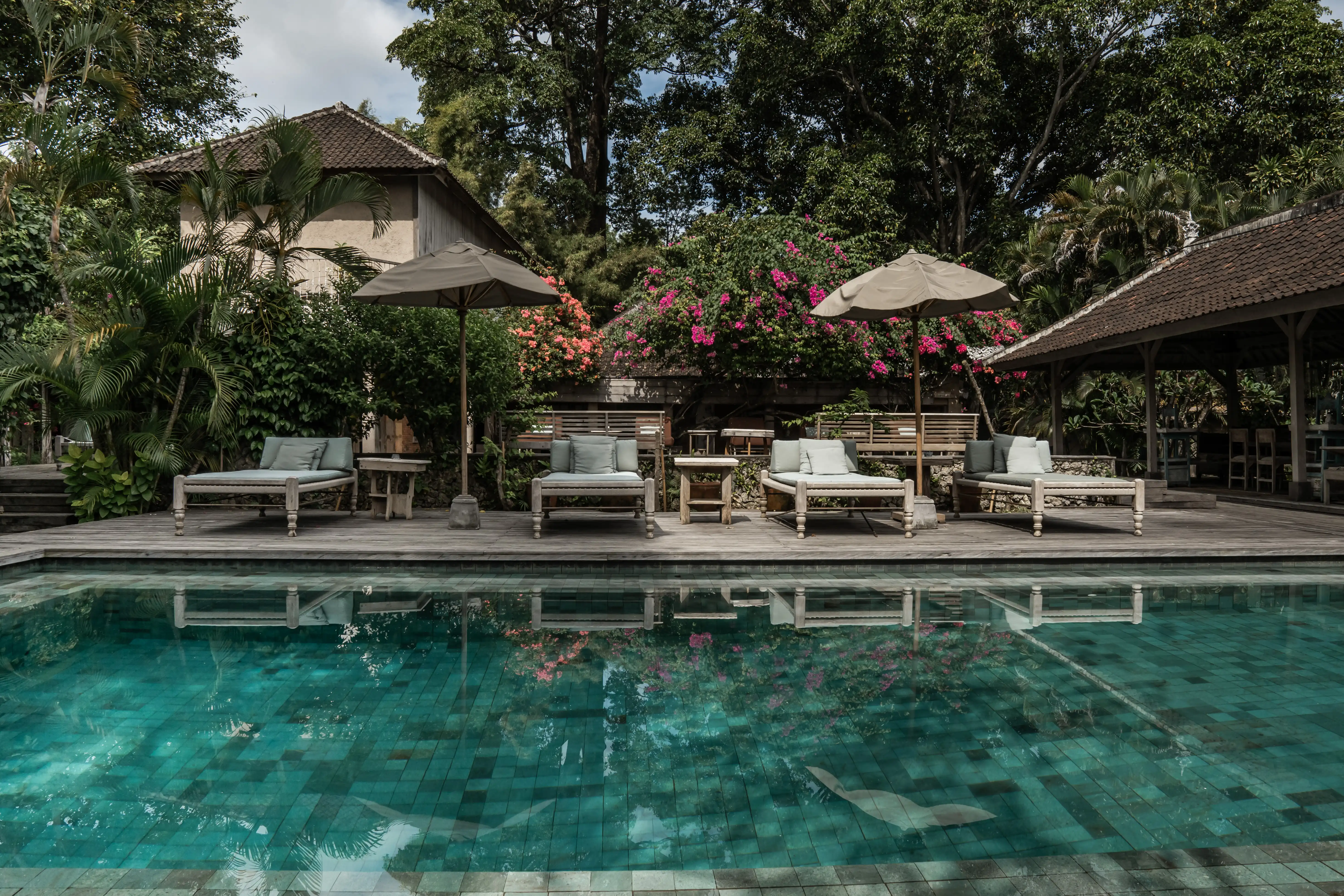 Outdoor swimming pool lined with sun loungers, parasols, and blooming bougainvillea at Balquisse Heritage Hotel in Jimbaran, Bali.