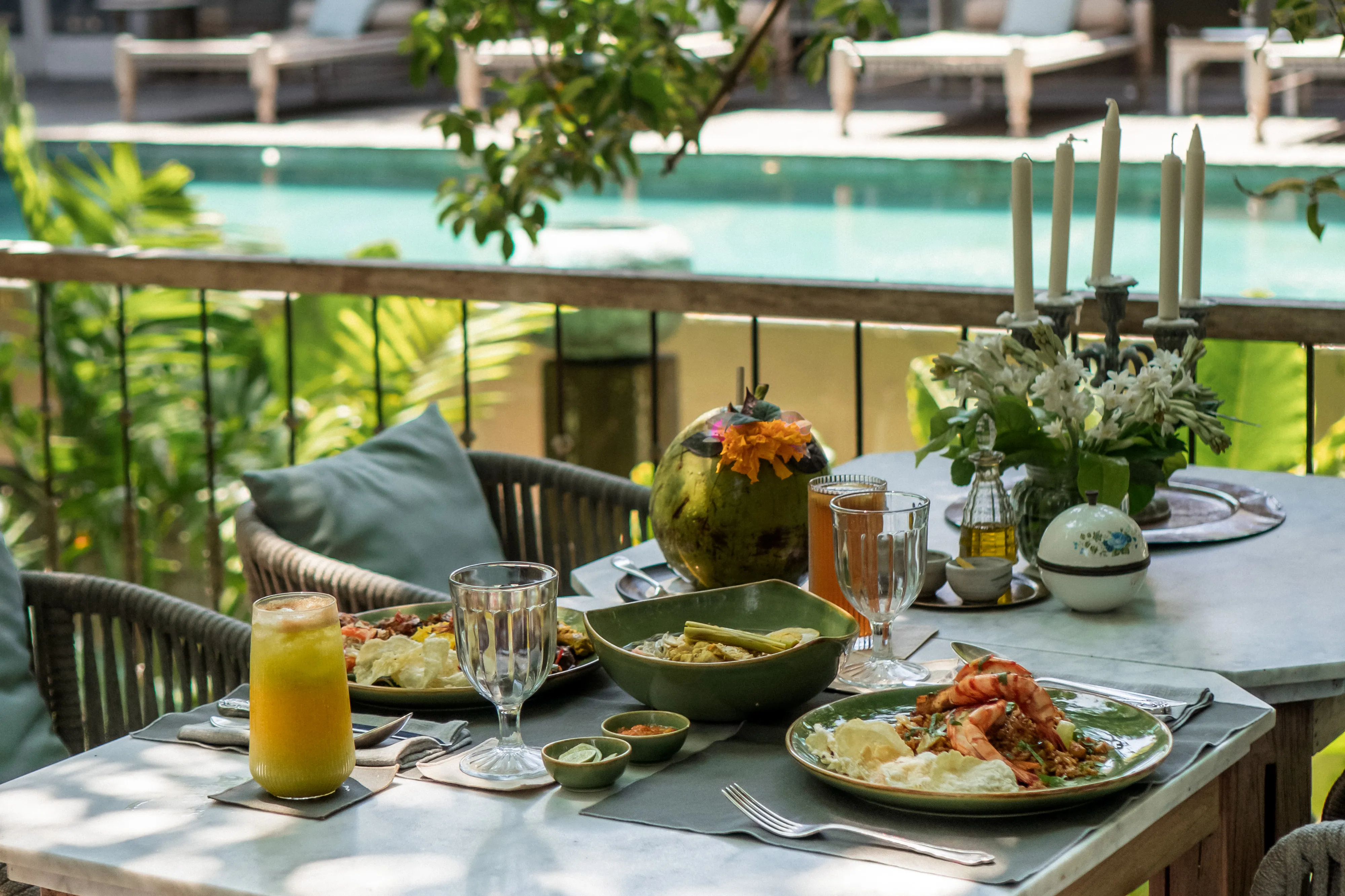 Outdoor dining setup with authentic Indonesian dishes, tropical drinks, and fresh coconut next to the swimming pool at Balquisse Heritage Hotel, Jimbaran, Bali.