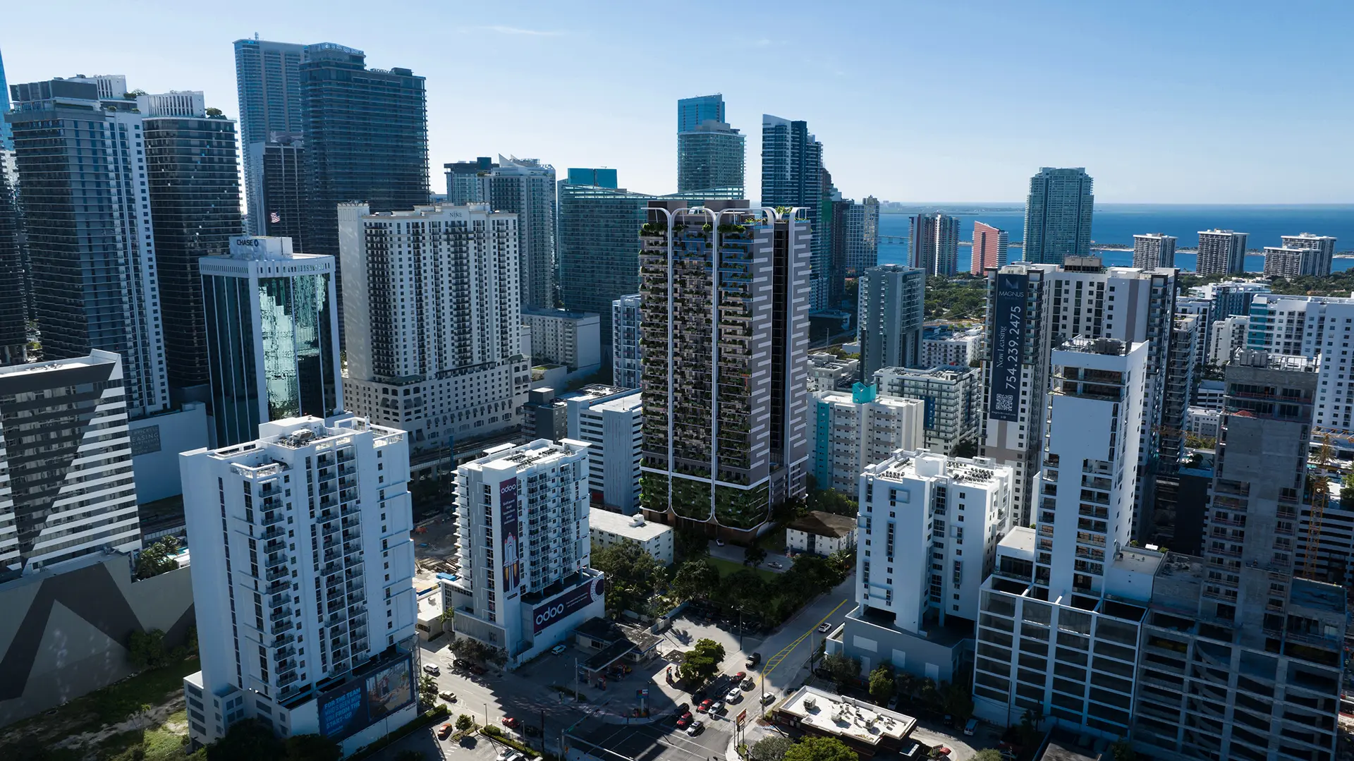  Aerial view of a green-balconied residential tower integrated into a dense Miami urban skyline with ocean views in the background.