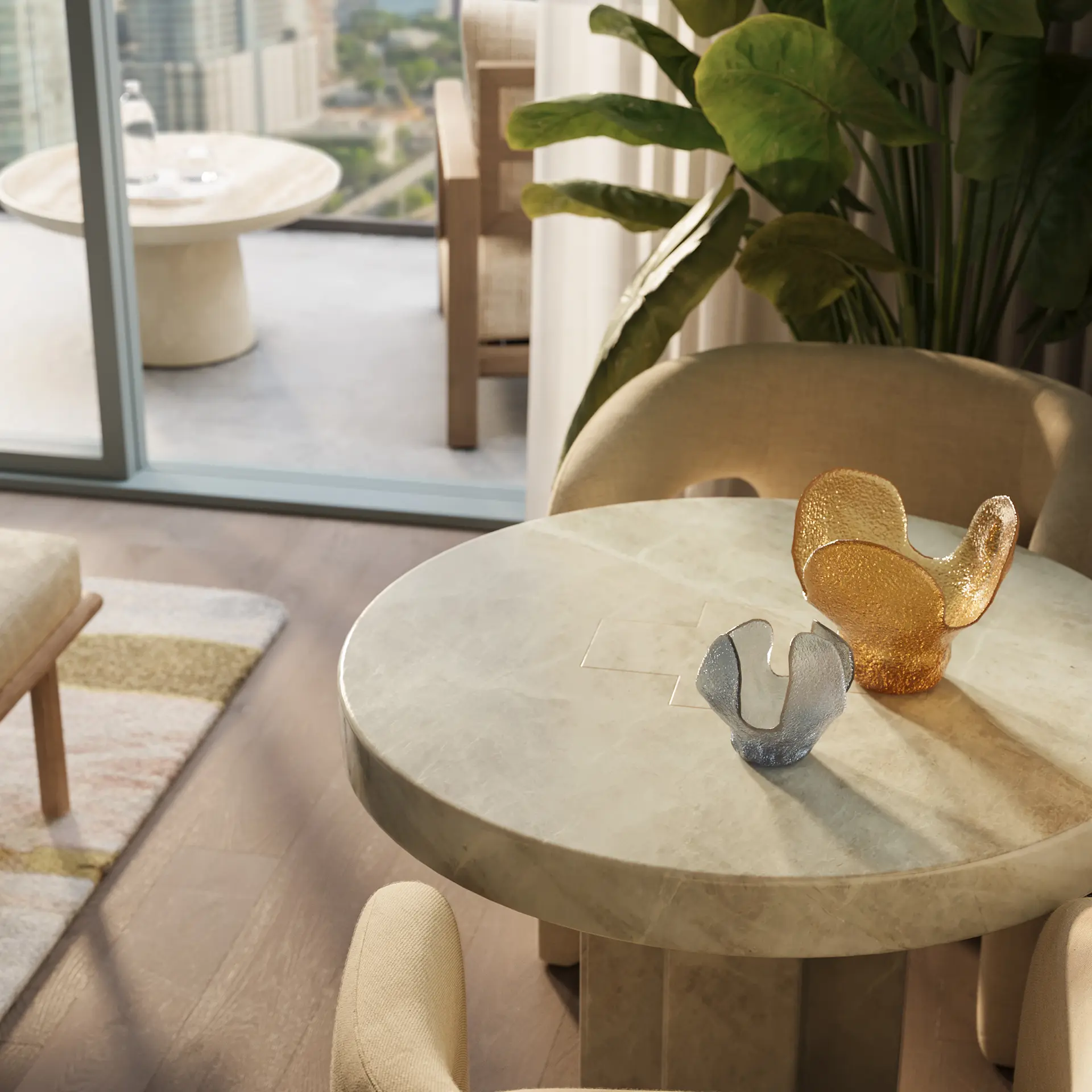 Round beige marble table with two textured glass sculptures, surrounded by beige chairs and green plant.