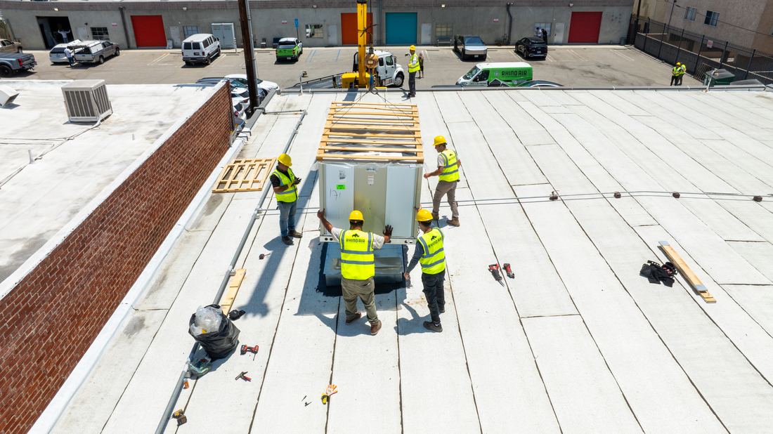 Rhino Air crew guiding a crane-set rooftop unit onto a media data center in Burbank — branded fleet on site
