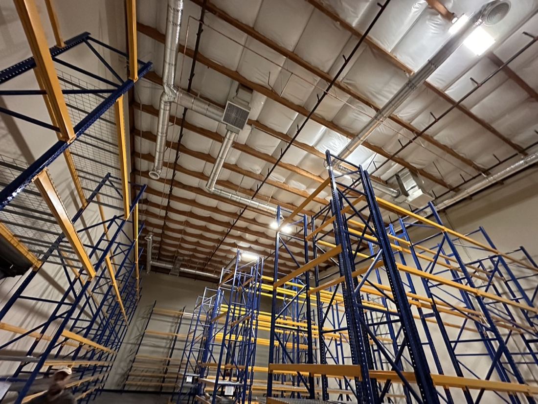 Exposed spiral ductwork above racking inside a temperature-controlled food production facility — HVAC by Rhino Air