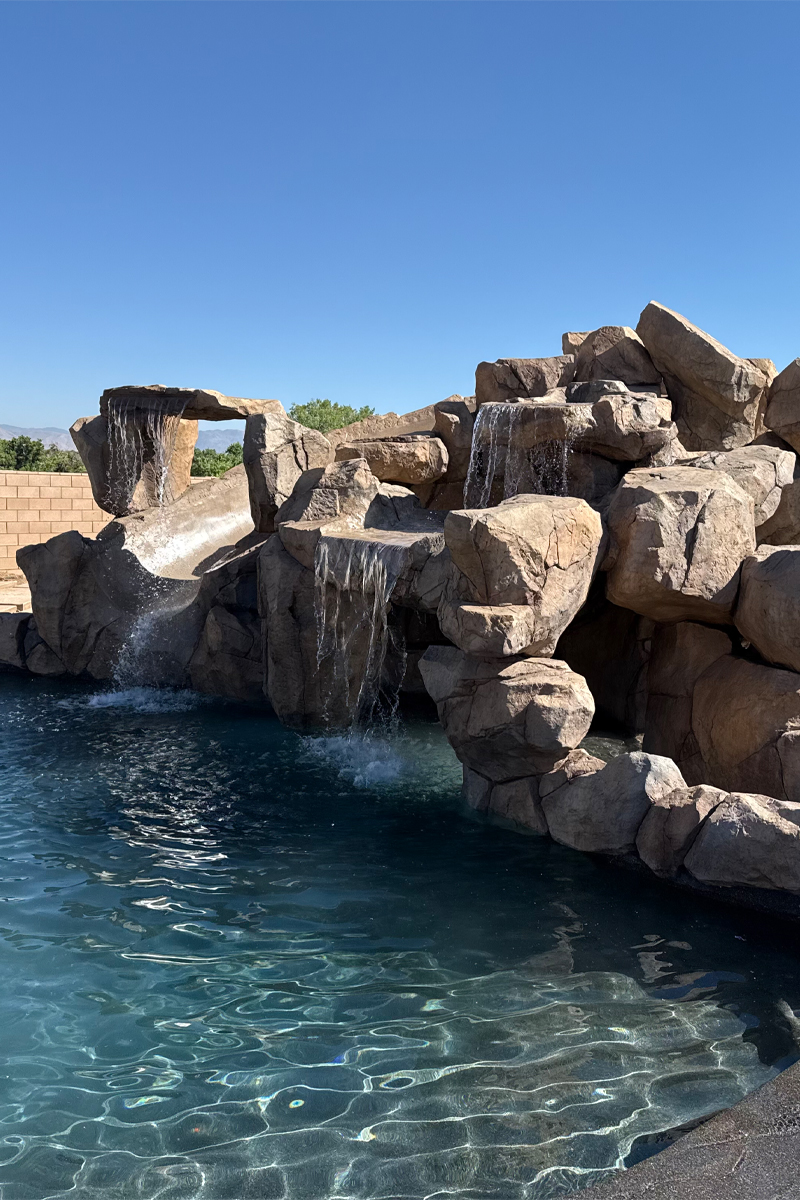 A beautiful swimming pool featuring a stone structure and three cascading waterfalls.