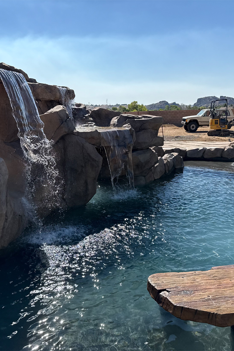 A beautiful swimming pool with cascading waterfalls in the background, along with a truck and a construction machine visible.