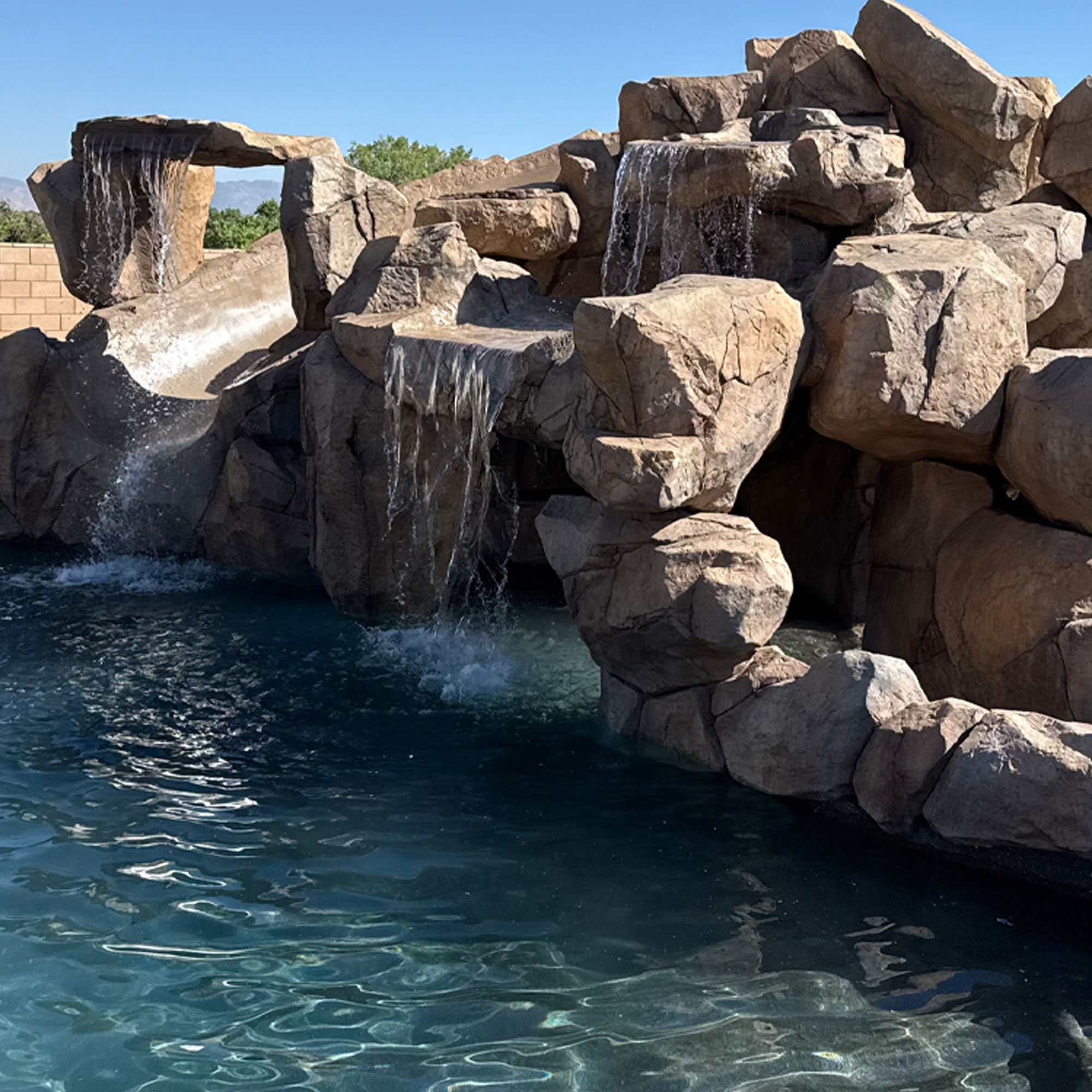 A swimming pool constructed entirely from stones, featuring three cascading waterfalls.