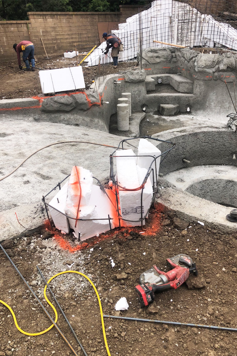 Construction workers are present alongside a structure made of iron bars and cement steps.

