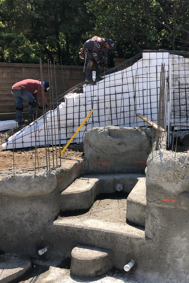 Construction workers are present alongside a structure made of iron bars and cement steps.