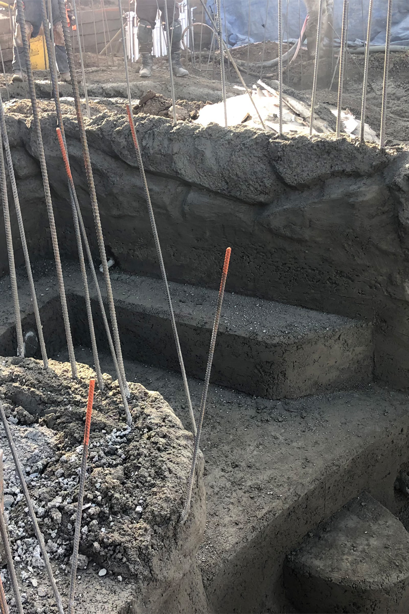 Iron bars are embedded into fresh, wet cement, likely for structural reinforcement.