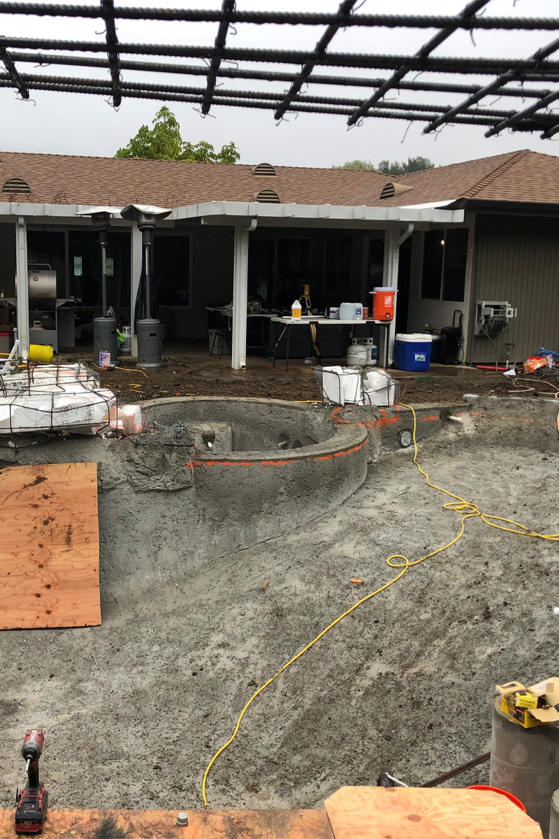 A swimming pool is under construction with fresh cement visible, and a house stands in the background.