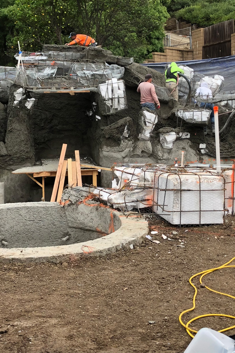 Workers are applying cement to a cave-like structure during its construction.
