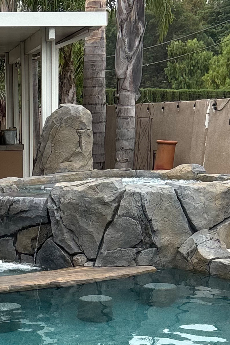 A jacuzzi constructed from stone, surrounded by the trunks of palm trees, creating a natural and tropical ambiance.