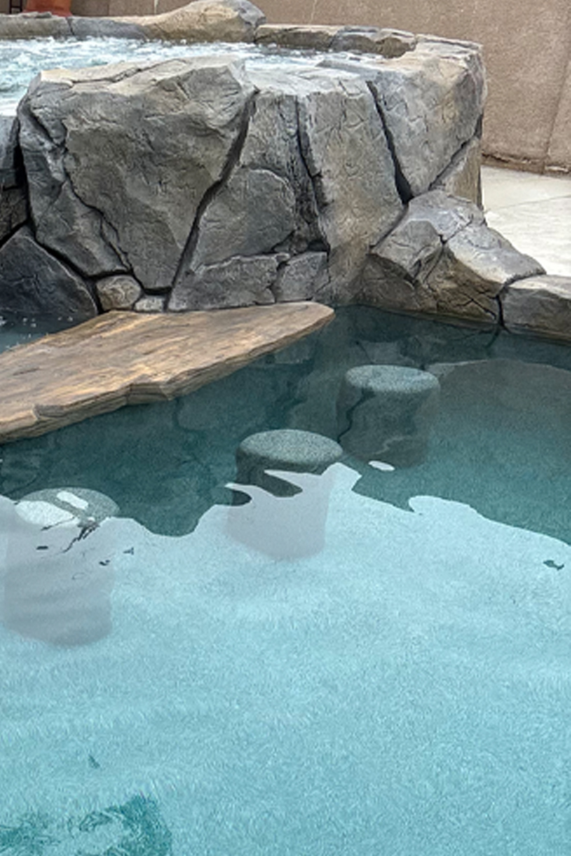 Cement seating built directly into a swimming pool, with an external wooden piece simulating a table, creating a functional and integrated design.
