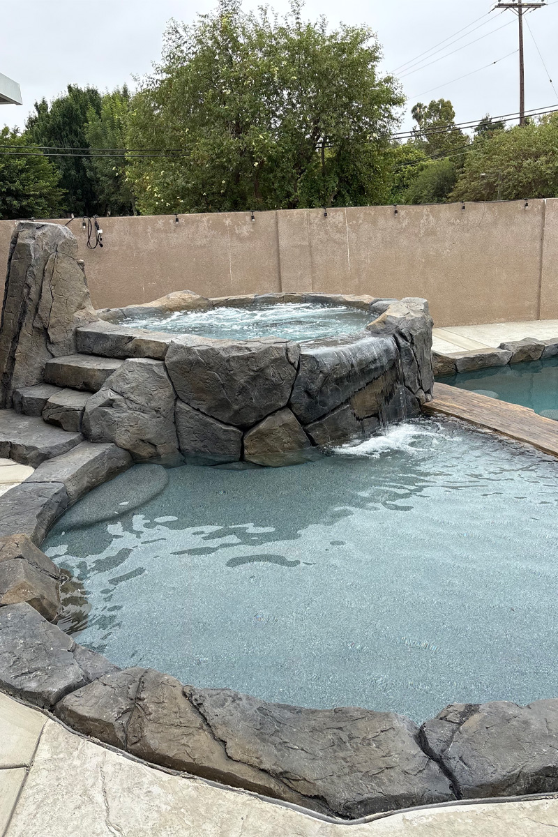 A beautiful jacuzzi made of stone, featuring built-in steps and a cascading waterfall.