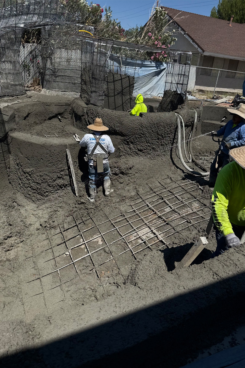 Workers are applying cement to a swimming pool that is currently under construction.