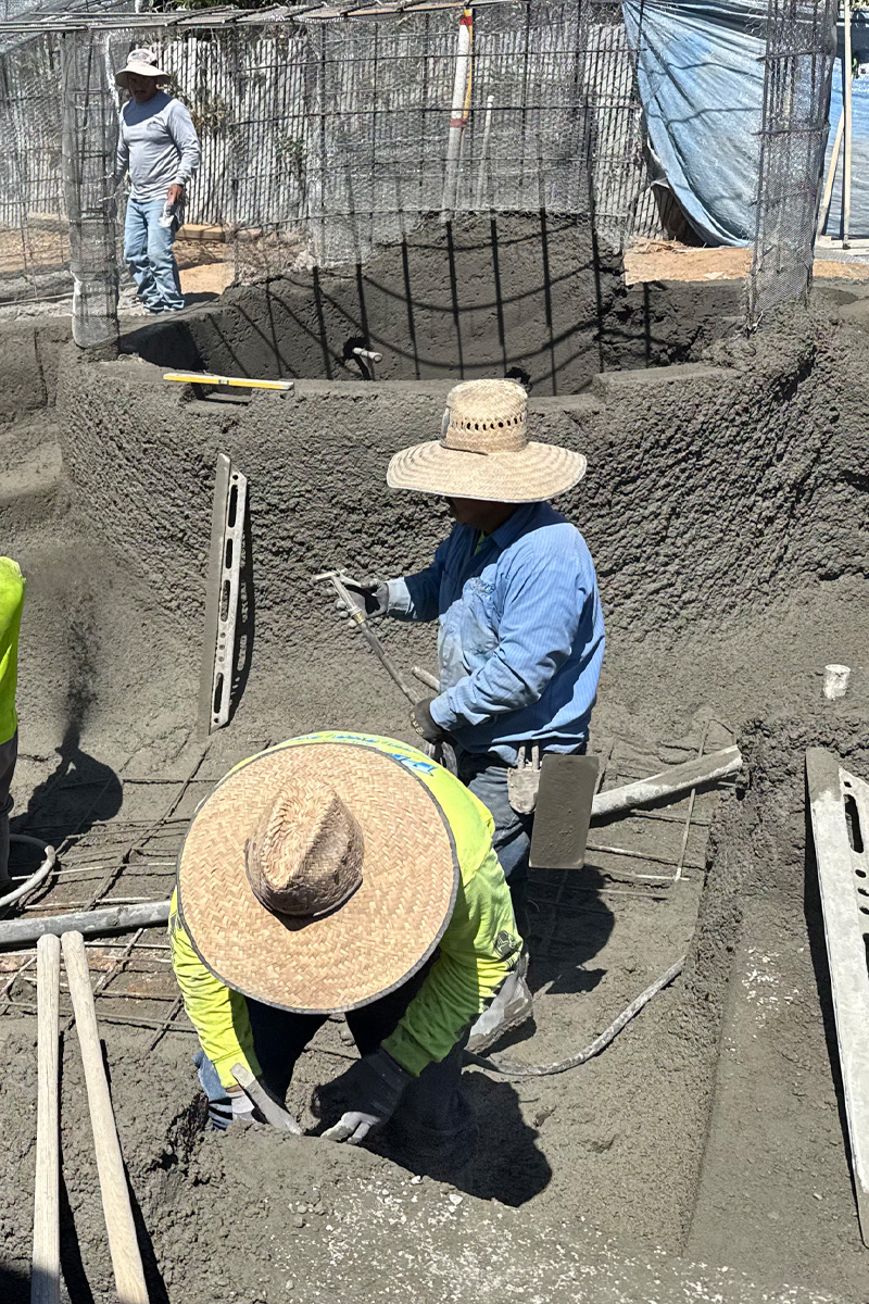Workers are actively pouring cement into a swimming pool during its construction.