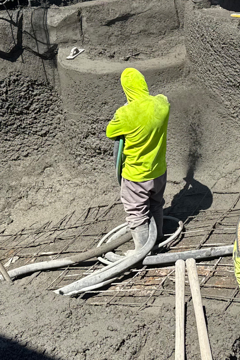 Worker are actively pouring cement into a swimming pool during its construction.