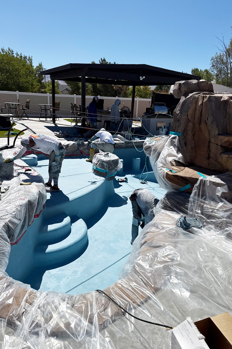 A swimming pool covered with plastic sheeting, while workers are engaged in painting around or within the pool area.