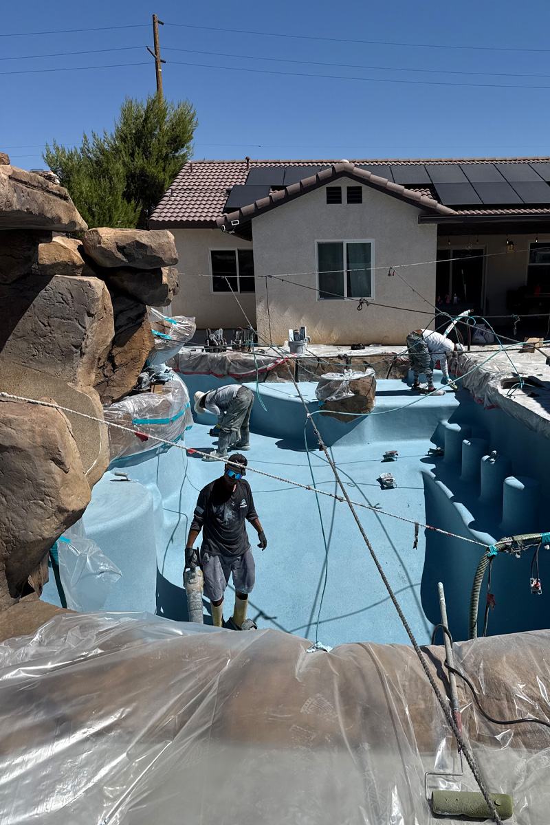 Three workers are painting a swimming pool a vibrant blue color.