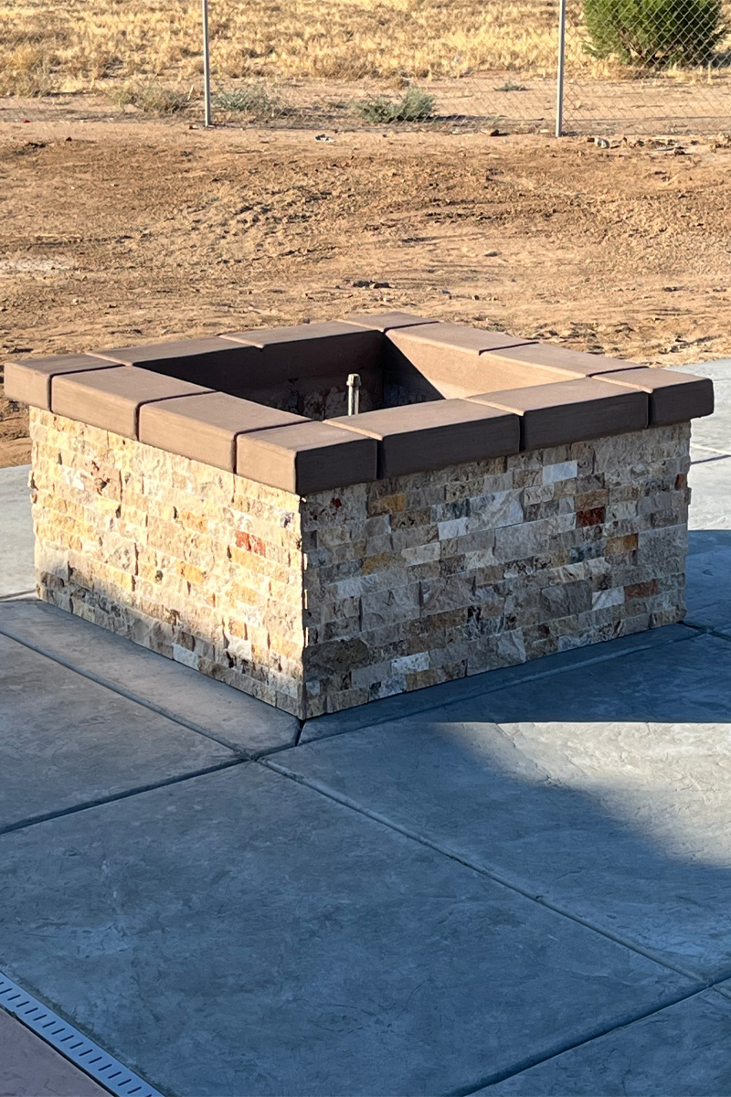 A fireplace in a nude or light, earthy tone, set on a cement patio with a dirt background.