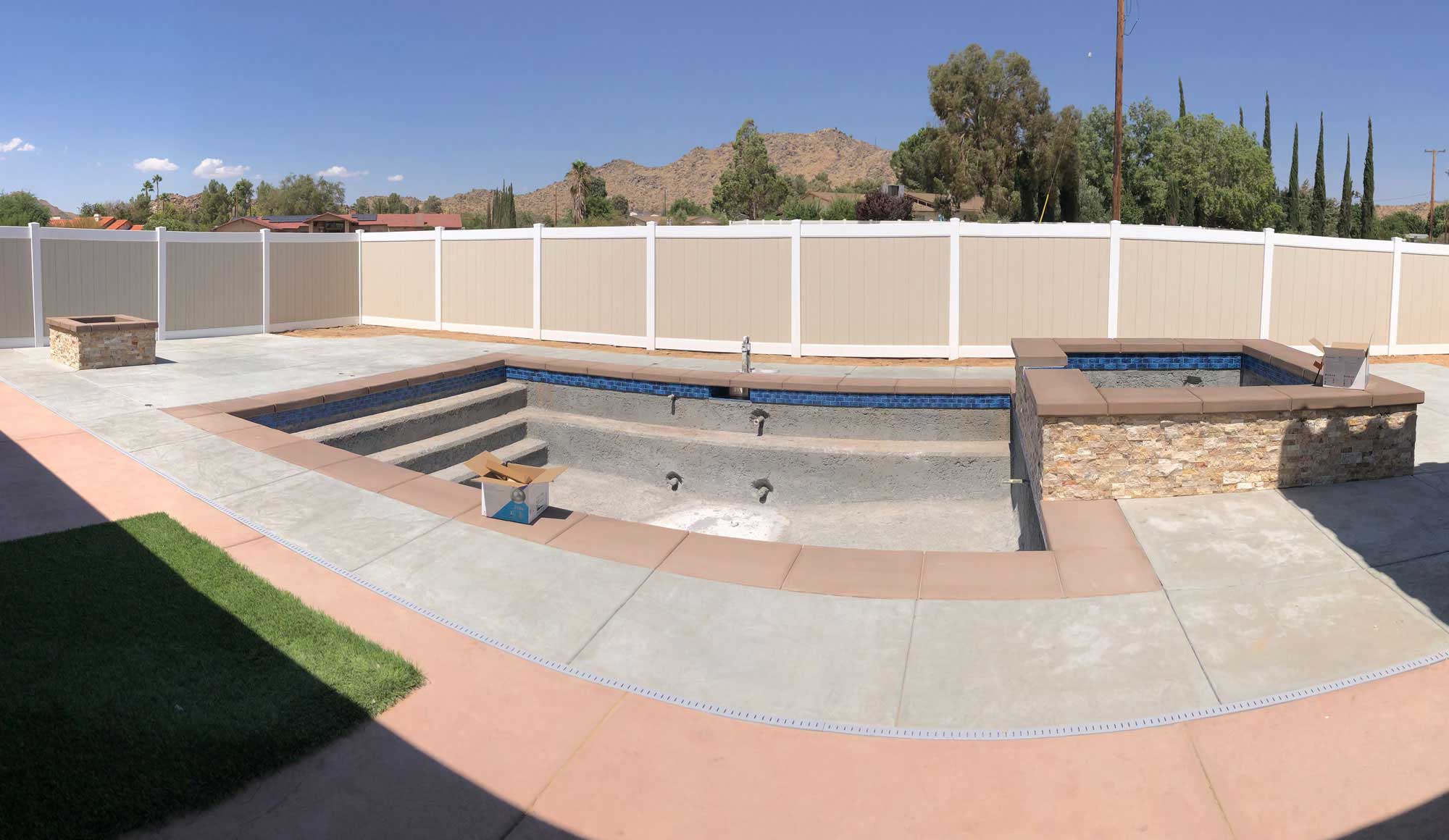 A swimming pool currently under construction, surrounded by a fence in a combination of beige and white colors.


