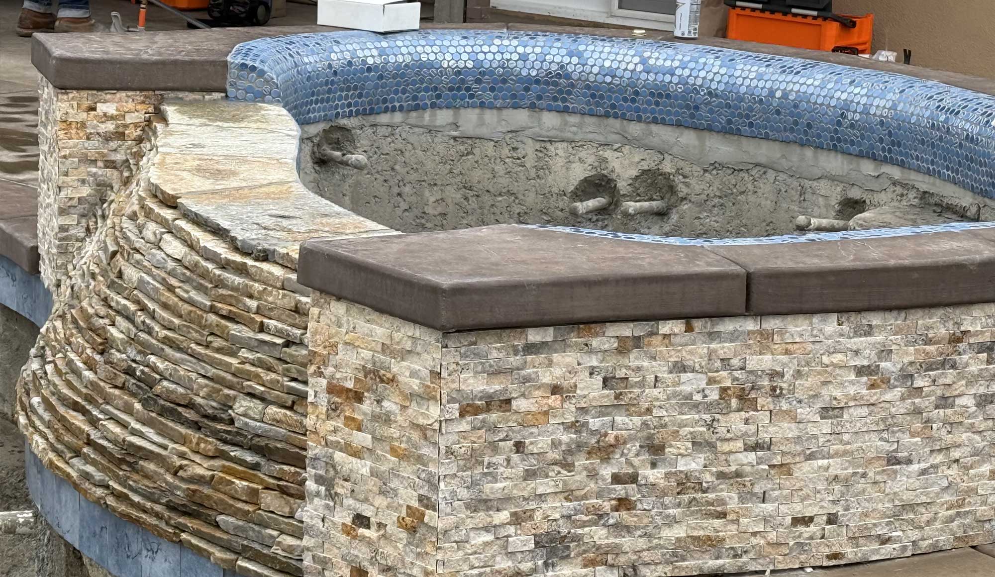 A jacuzzi currently under construction, featuring intricate mosaic tiles in shades of blue and earthy tones.