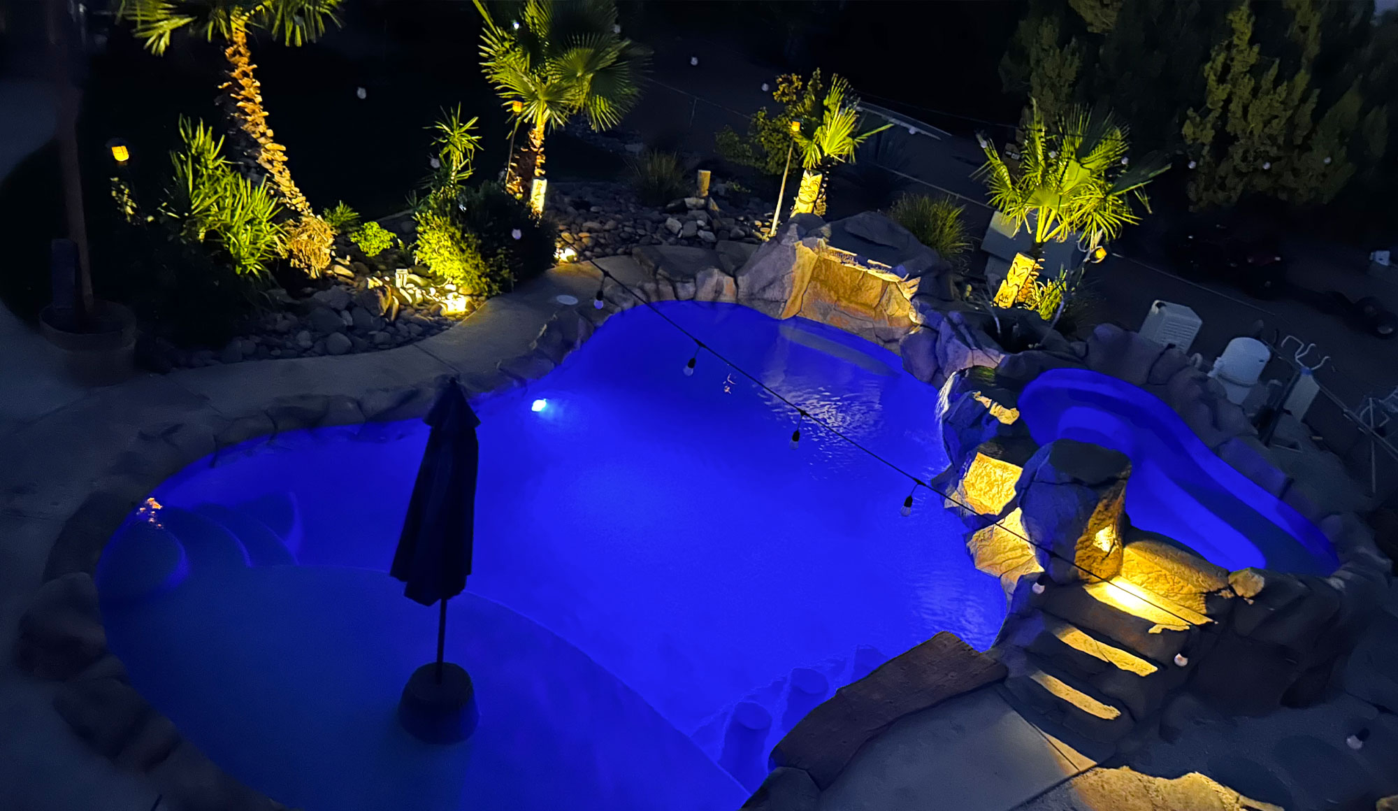 An overhead view of a swimming pool, perfectly illuminated with a vibrant blue glow.

