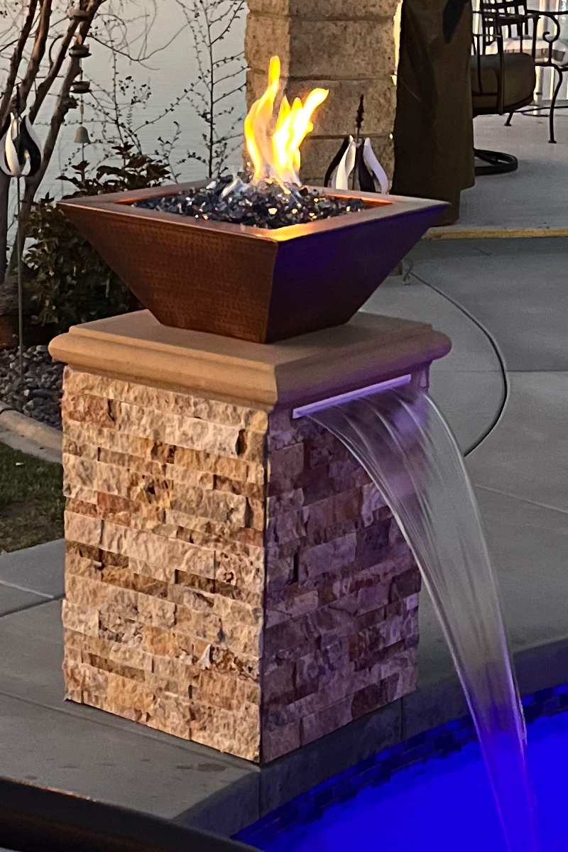 A small waterfall seamlessly integrated into a swimming pool, featuring a fire element above it