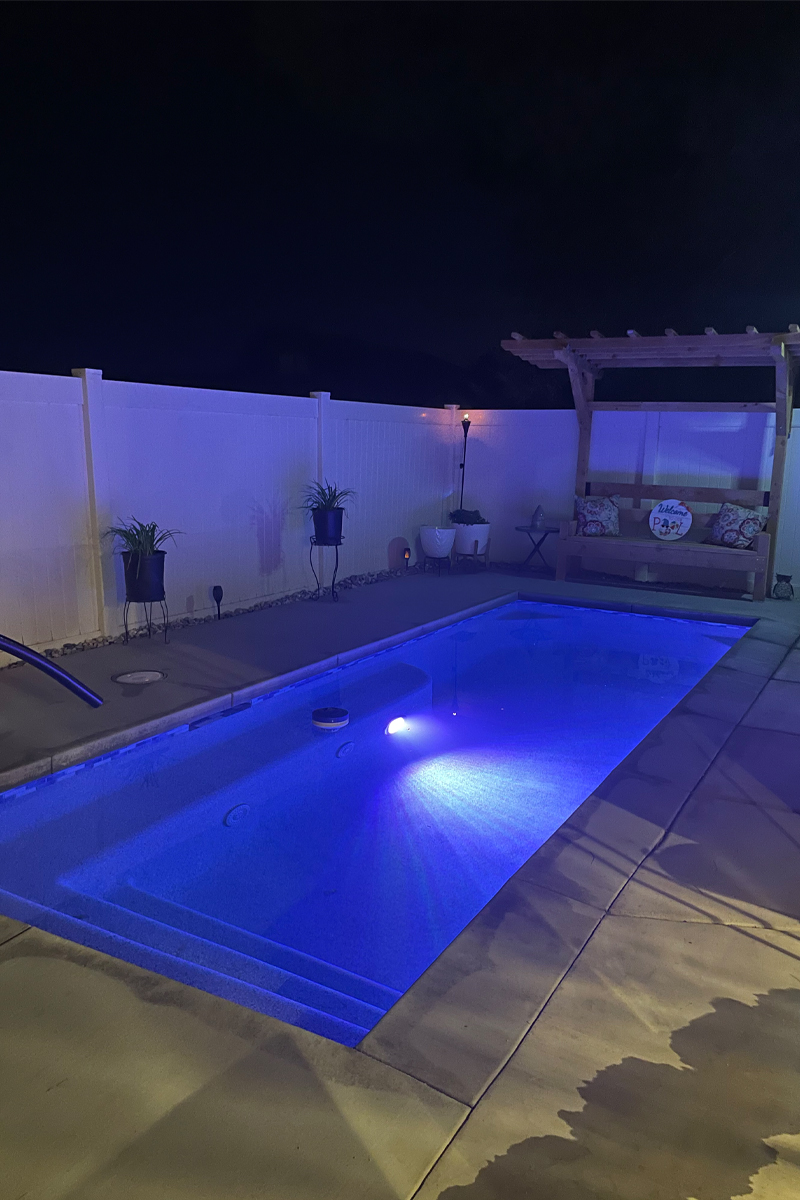 A square swimming pool with elegant lighting, accompanied by a decorative covered bench or seating area.