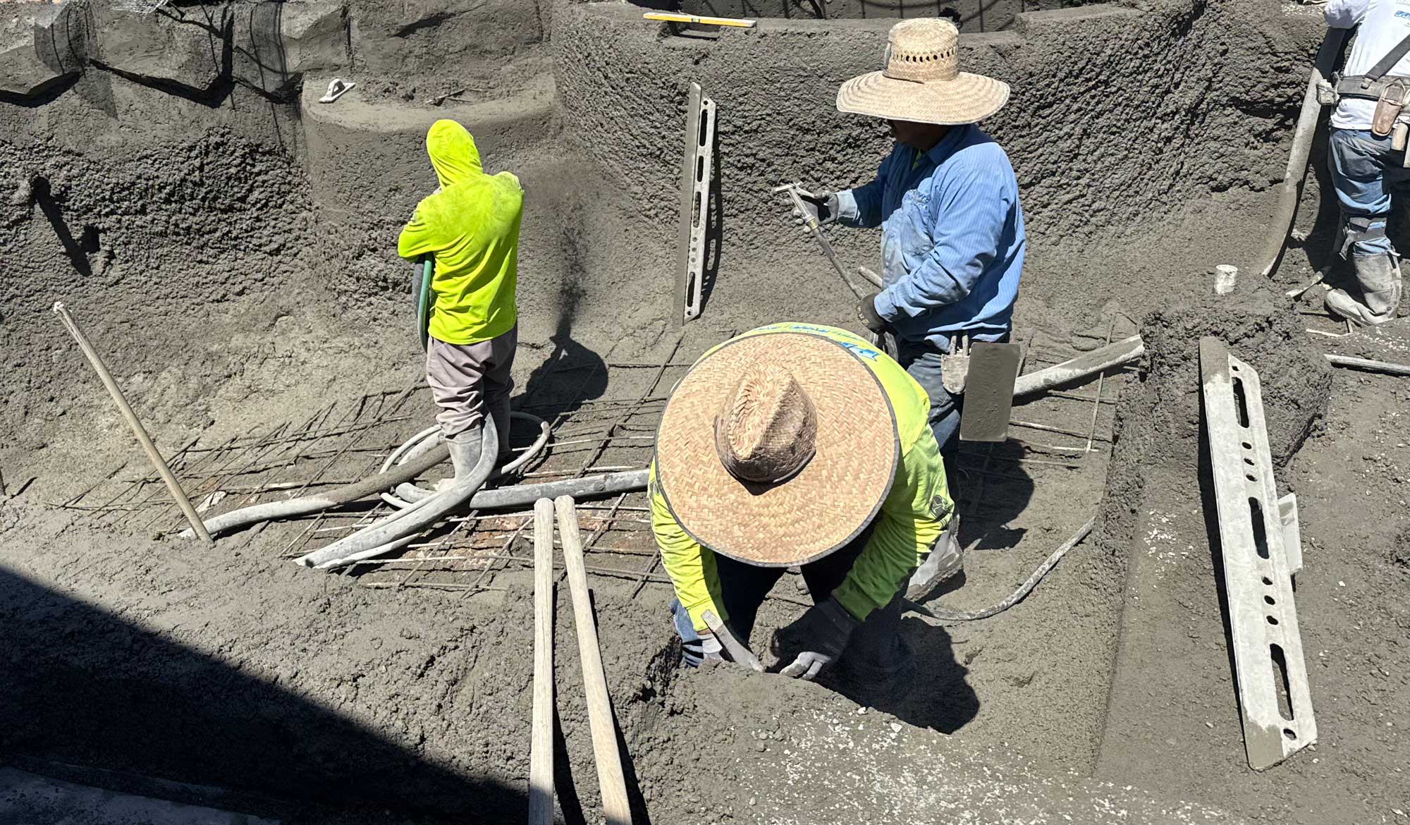four men are actively working on the construction of a swimming pool. They are working with fresh cement and reinforcing it with iron rebar.