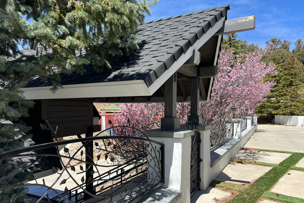 A beautiful, intricate entrance crafted from dark metal, featuring decorative figures and designs. The entrance is covered by a roof made of dark grey tiles