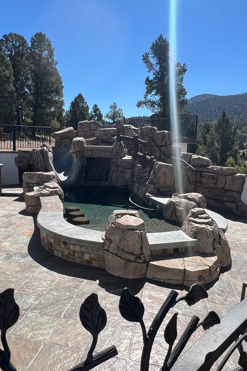 A beautiful swimming pool crafted from natural stones, offering a stunning view of a lush mountain covered with abundant pine trees.