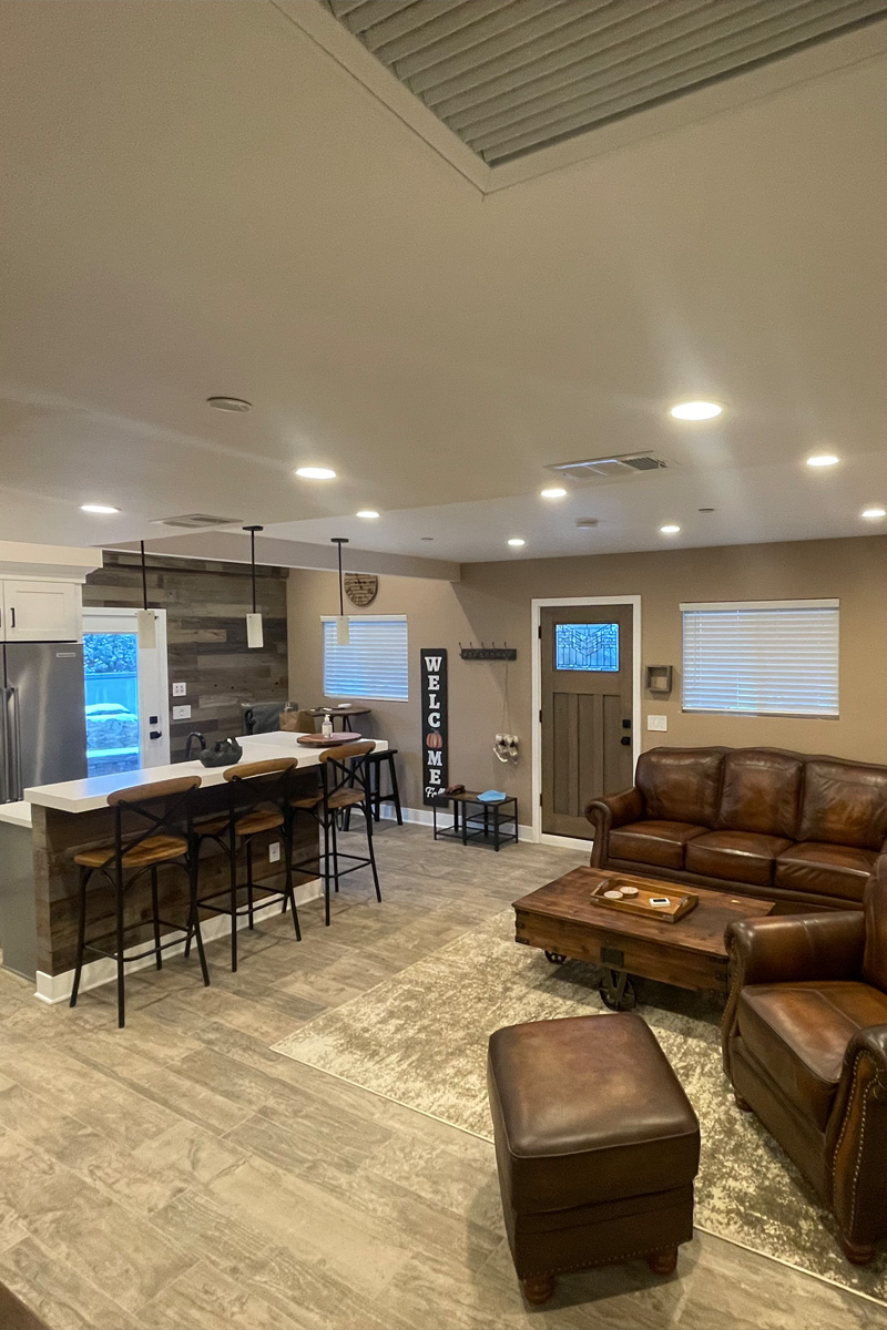 A sophisticated and elegant living room featuring luxurious camel-colored leather sofas and various wooden accessories. This open-concept space flows seamlessly into an adjacent kitchen.