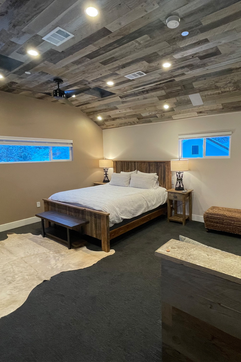 An elegant bedroom featuring a sophisticated grey wooden ceiling. The room is furnished with a stylish wooden bed, and a lamp is placed on each side of the bed, providing symmetrical lighting.