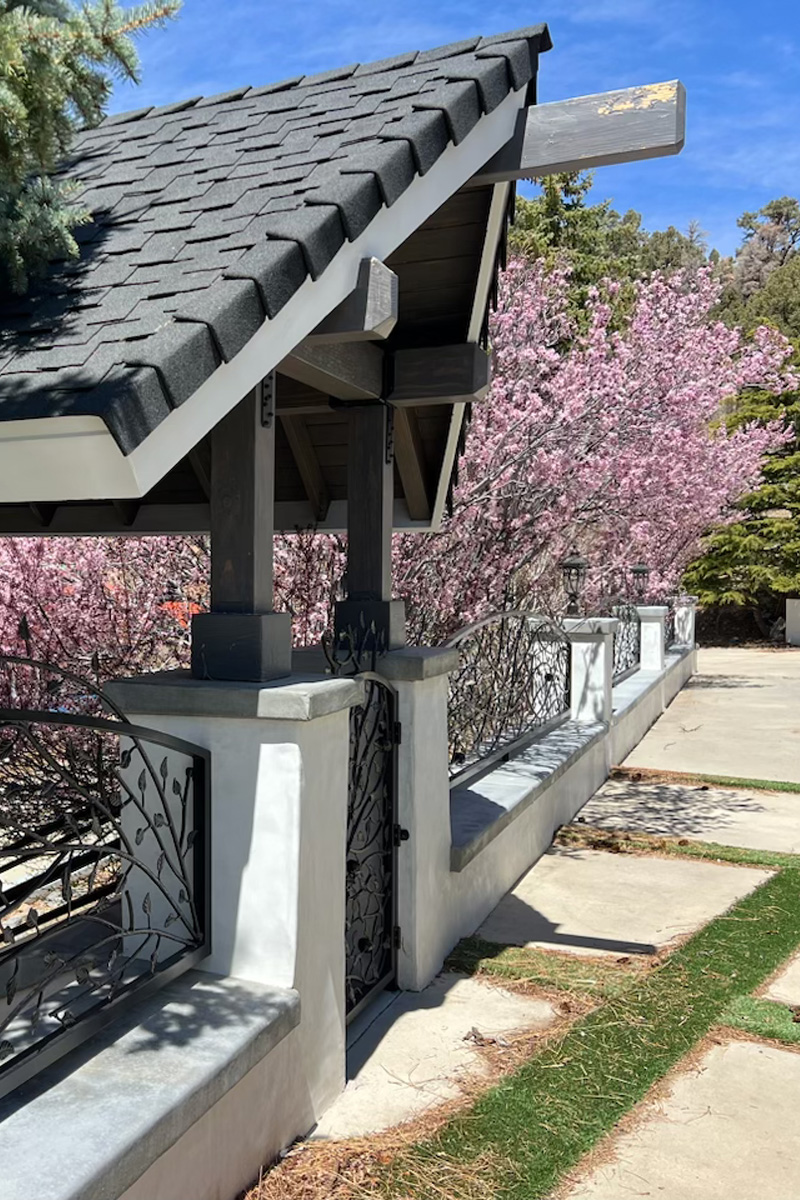 A beautiful, intricate entrance crafted from dark metal, featuring decorative figures and designs. The entrance is covered by a roof made of dark grey tiles