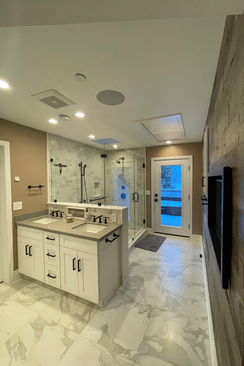A luxurious bathroom with a double vanity featuring two sinks. In the background, there is a large shower enclosure. The room is decorated in a minimalist style with a neutral, nude color palette.

