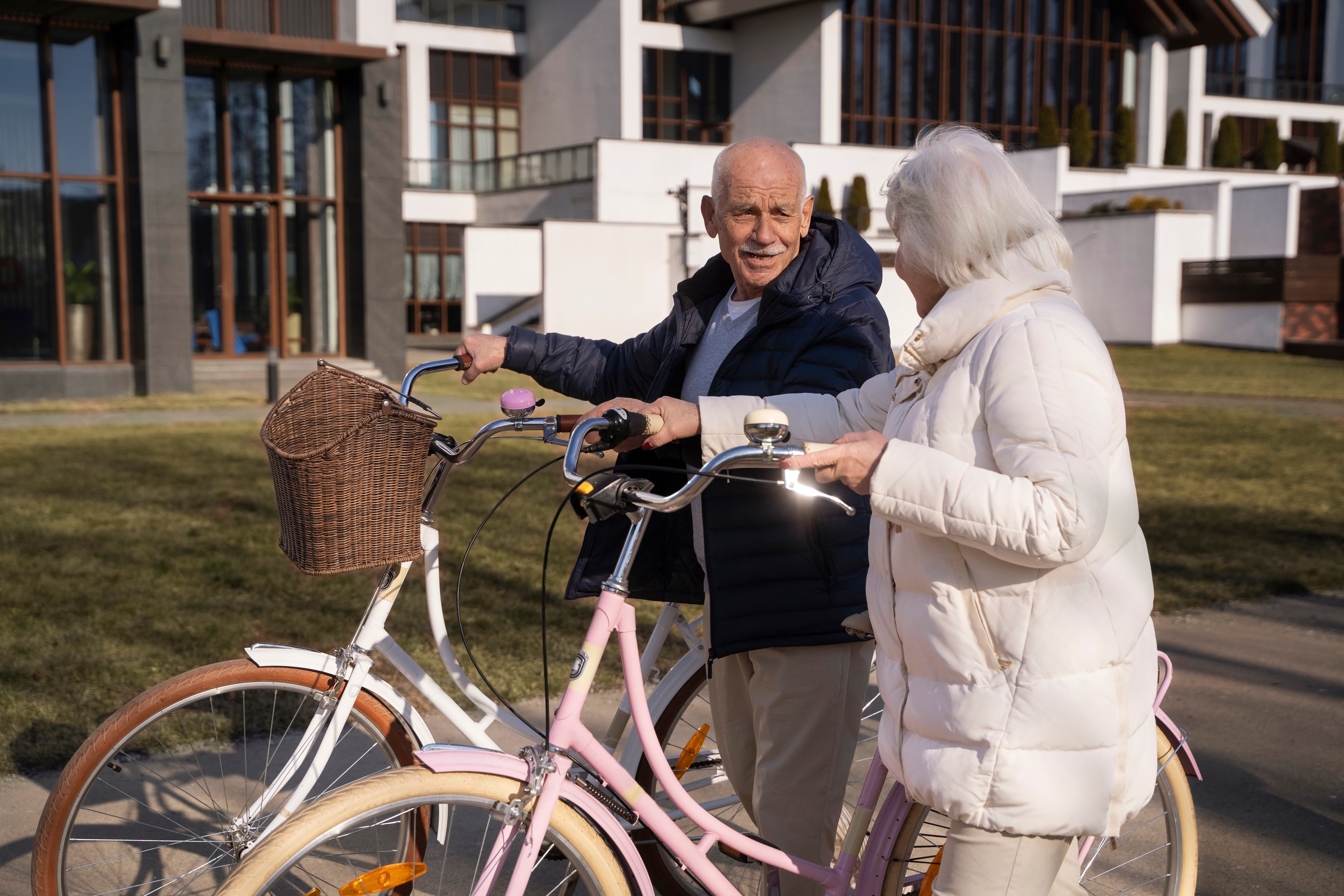 Elderly couple with bicycles chatting outside a modern building on a sunny day.