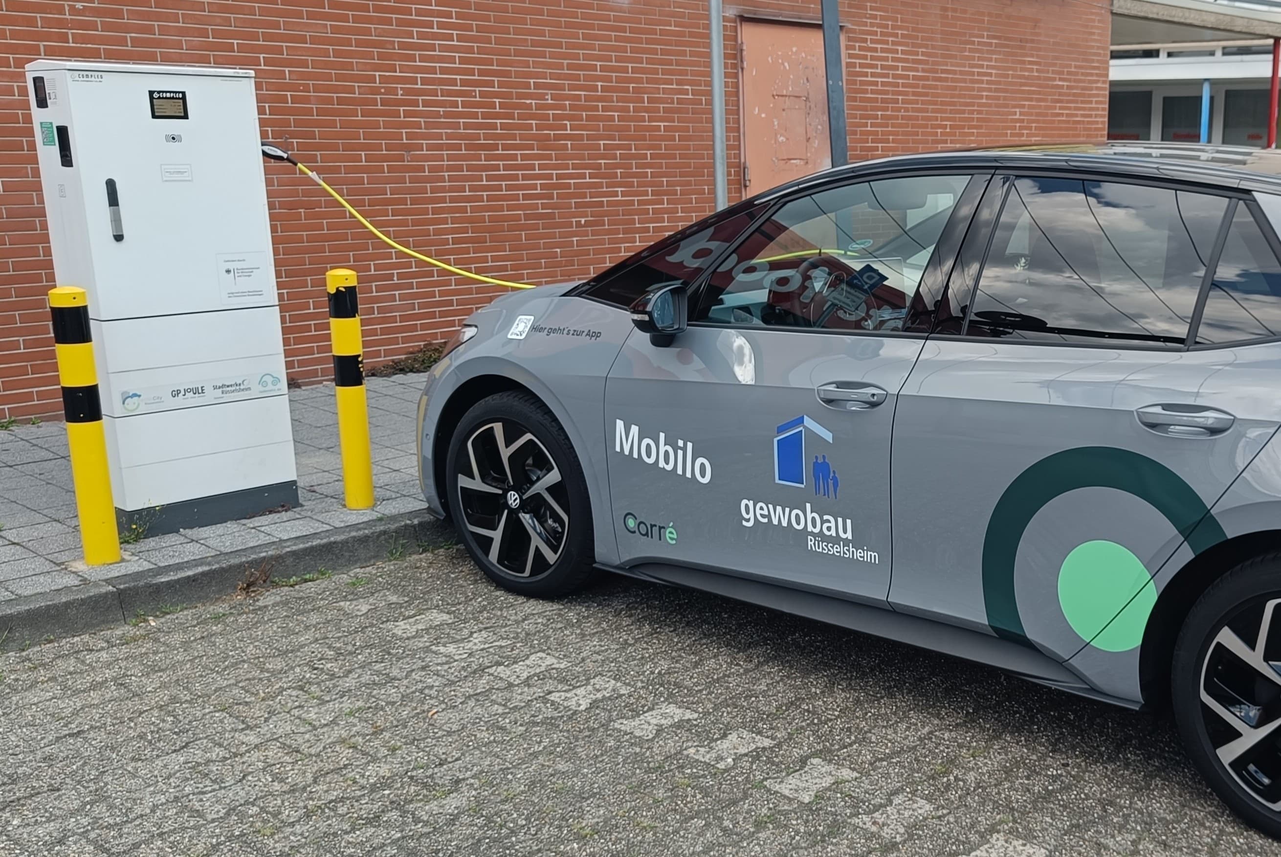 Gray electric car labeled Mobilo gewobau Rüsselsheim parked and charging at a white station.