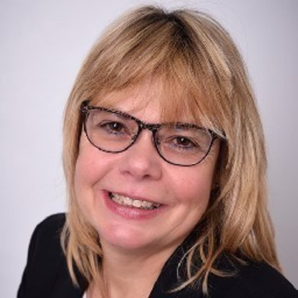 Smiling woman with blonde hair wearing glasses and a black top against a plain background.