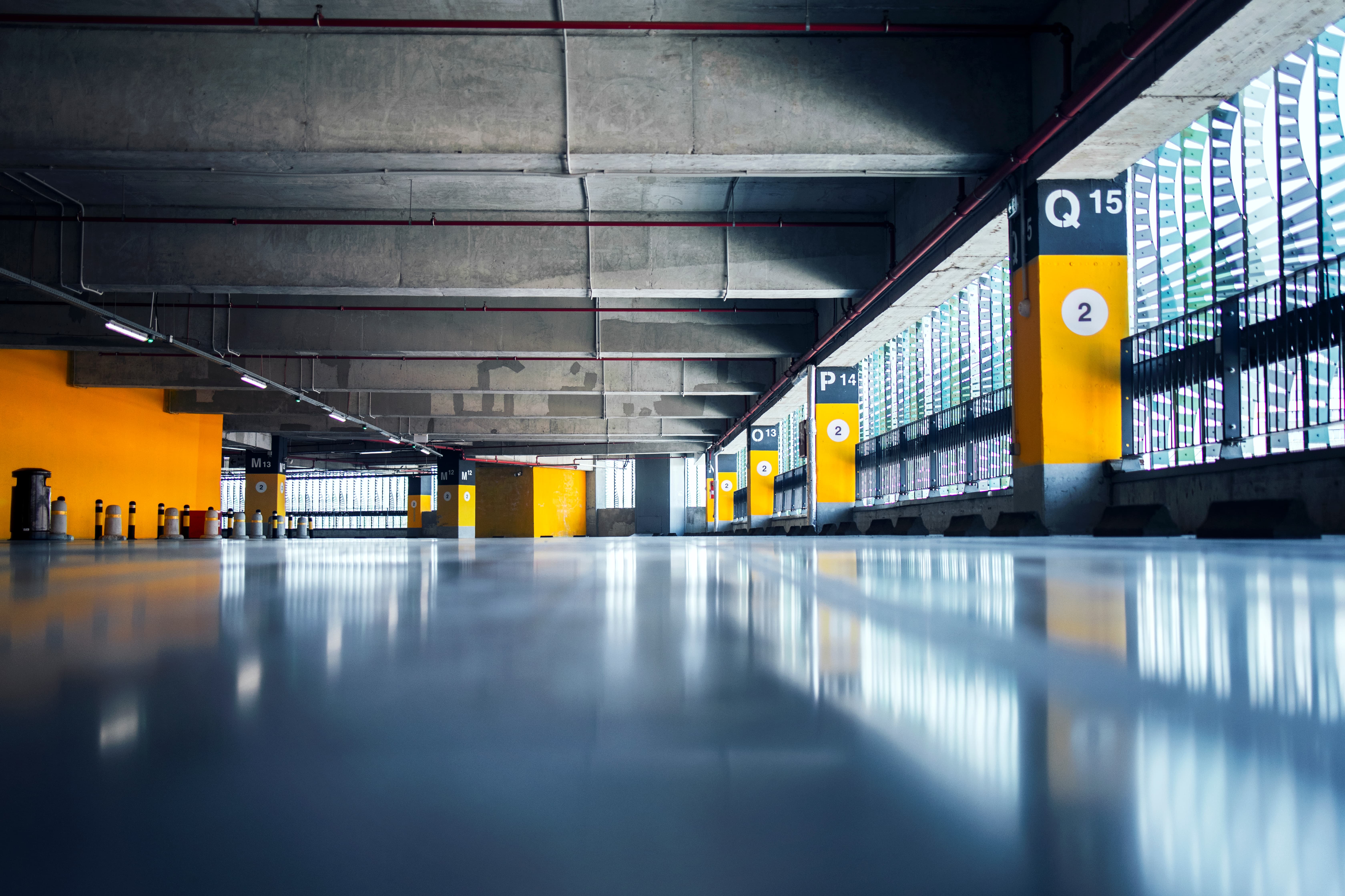 Empty indoor parking garage with yellow and gray pillars numbered and large windows on the right.