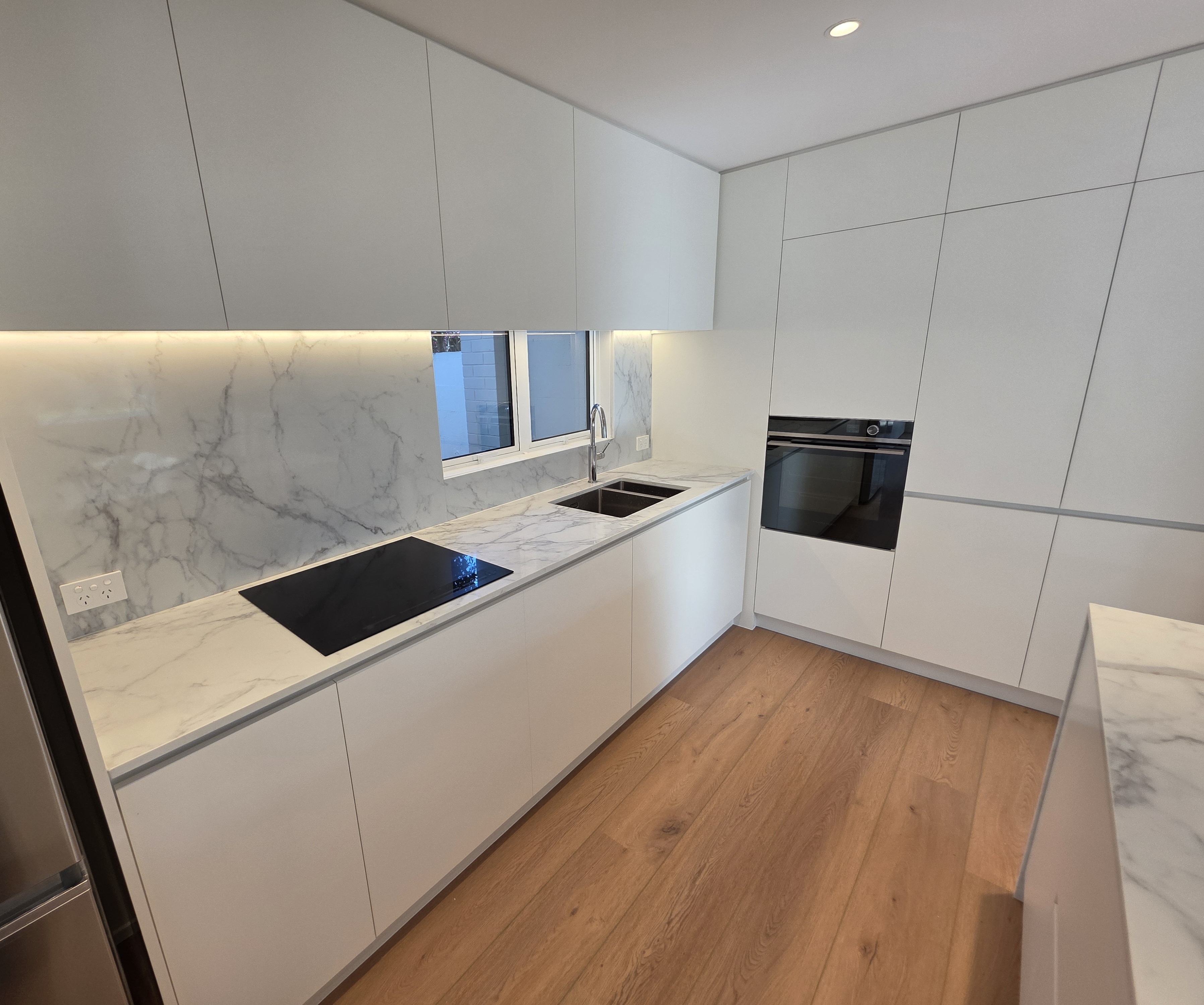 Modern white kitchen with marble splashback, under-cabinet lighting and built-in oven
