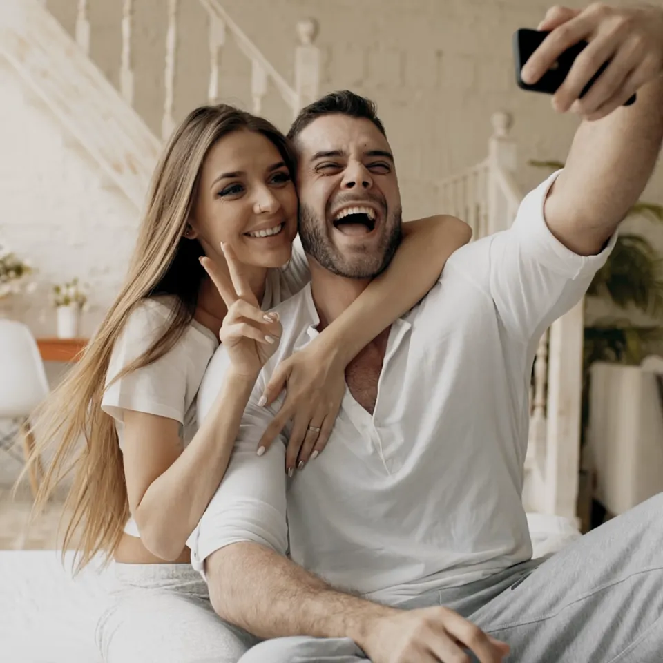 Ein Paar macht zusammen ein Selfie, die Frau zeigt ein Peace-Zeichen und beide lachen.