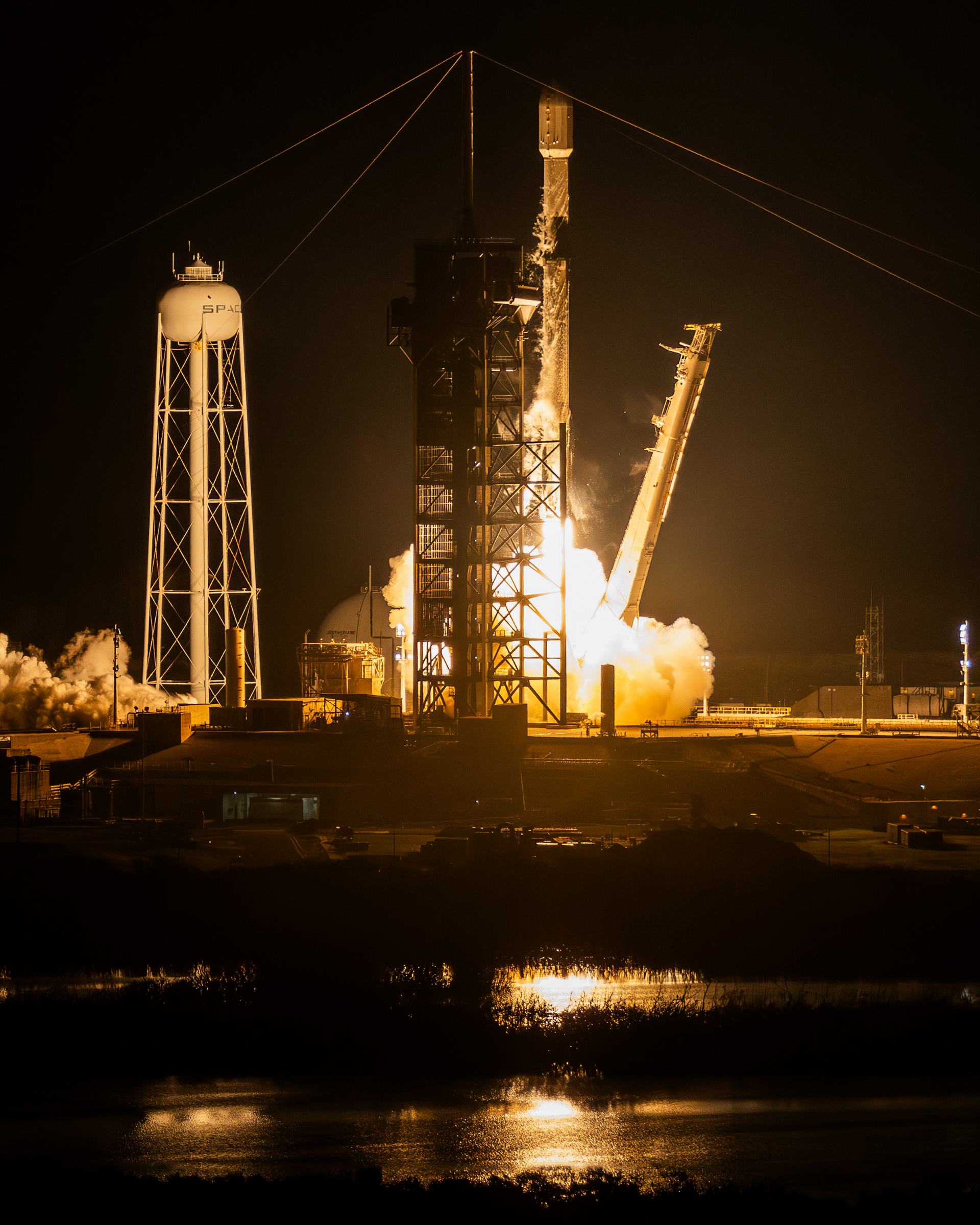 A night launch seen through the lattice of pad structures, the exhaust lighting the surrounding towers.