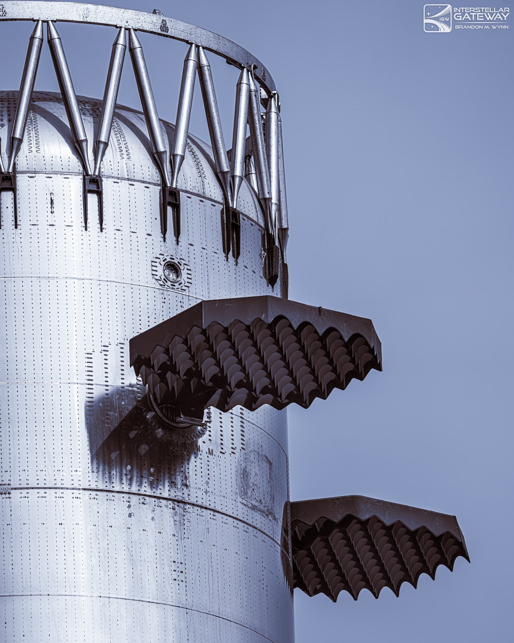 The grid fins of a Super Heavy booster folded against the stainless hull.