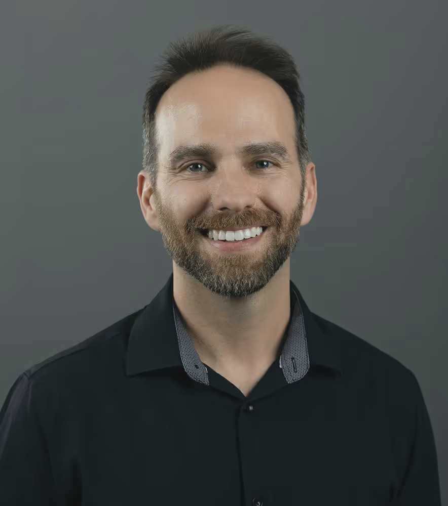 Smiling man with a beard wearing a black shirt against a gray background.