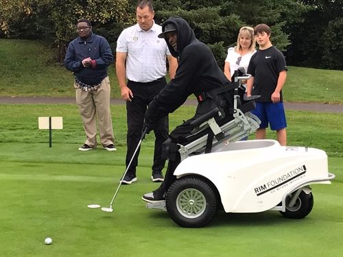 Man using a paragolfer putts while his instructor and three people watch.