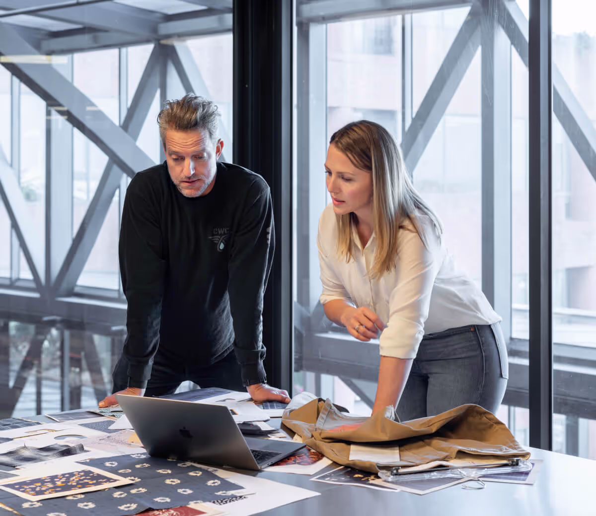 Un homme et une femme debout autour d'une table de travail consultent ensemble un ordinateur portable