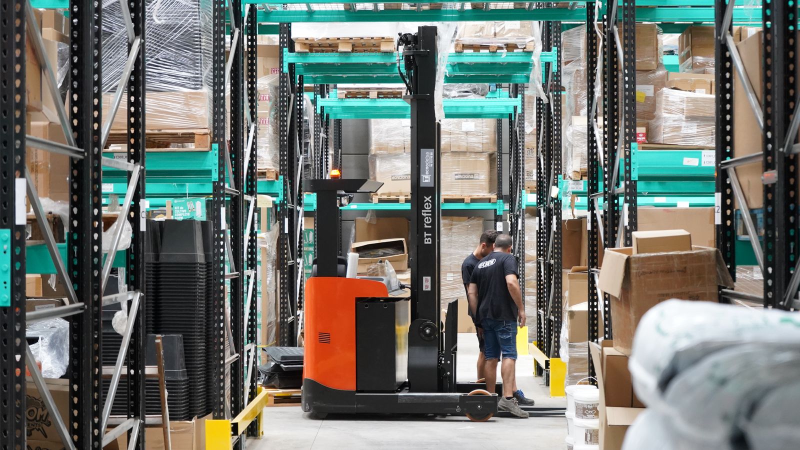 Un chariot élévateur circule dans les allées d'un entrepôt où travaillent plusieurs salariés